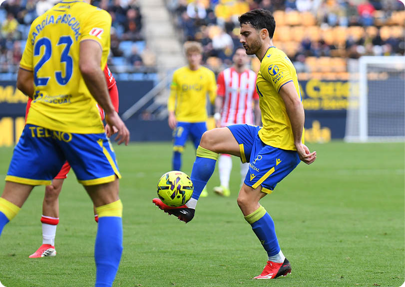 A soccer player in a yellow and blue uniform is kicking a soccer ball on a field. Contenido generado con IA