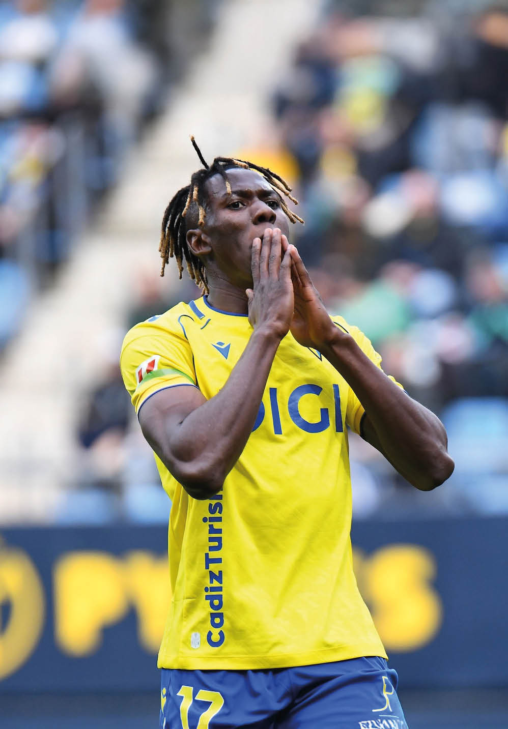 A soccer player with dreadlocks and a yellow shirt is praying on the field. Contenido generado con IA