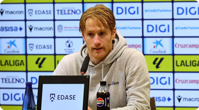 A man in a grey hoodie is sitting at a desk with a Pepsi bottle in front of him. Contenido generado con IA