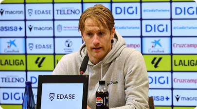 A man in a grey hoodie is sitting at a desk with a Pepsi bottle in front of him. Contenido generado con IA