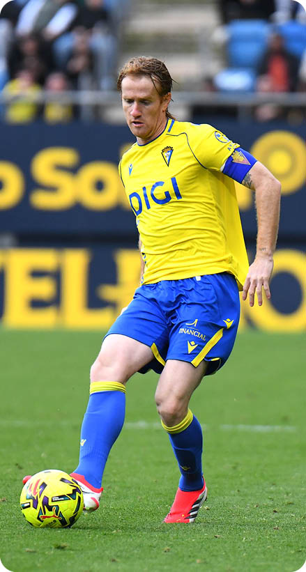 A soccer player in a yellow and blue uniform is about to kick the ball. Contenido generado con IA