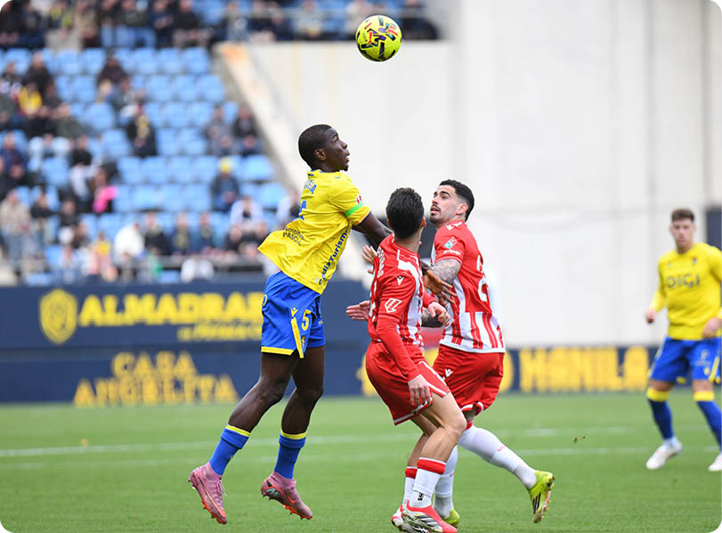 Three soccer players are on the field, with one player jumping in the air to head the ball. The other two players are trying to defend against the attack. Contenido generado con IA