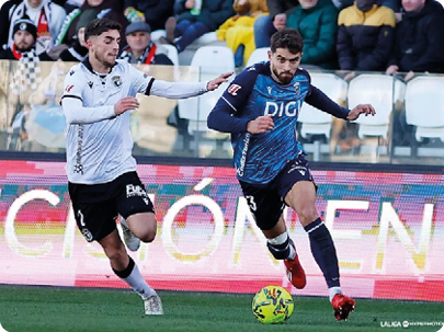 Two soccer players are running towards the ball on the field. Contenido generado con IA