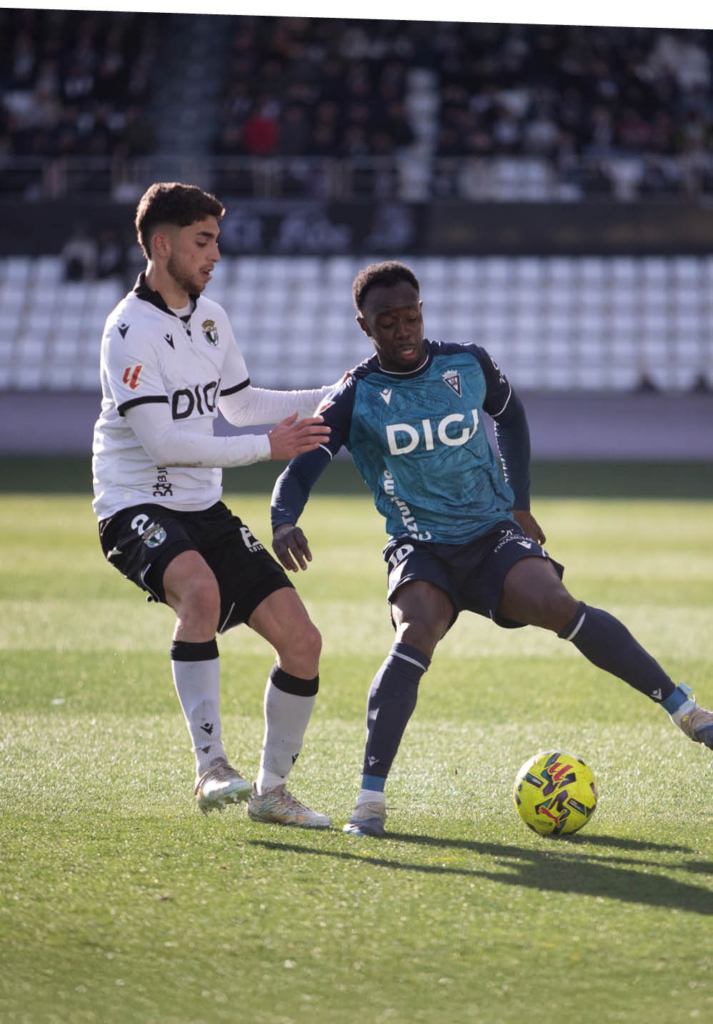 Two soccer players are playing on a field, one in a white and black uniform and the other in a blue and white uniform. The players are trying to gain control of the soccer ball. Contenido generado con IA