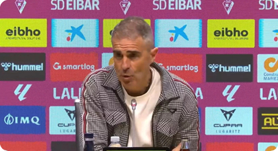 A man wearing a white shirt and a plaid jacket is sitting in front of a microphone. Contenido generado con IA