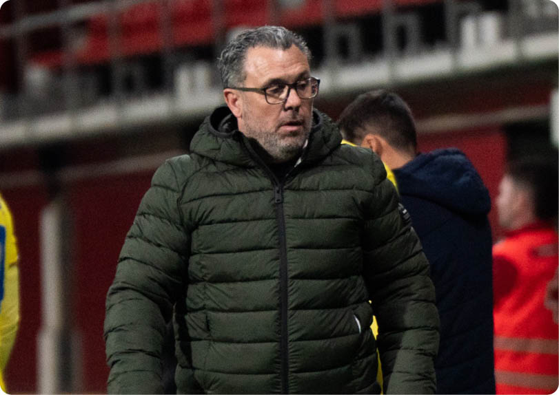 A man in a green jacket is walking on a field with a soccer ball. Contenido generado con IA