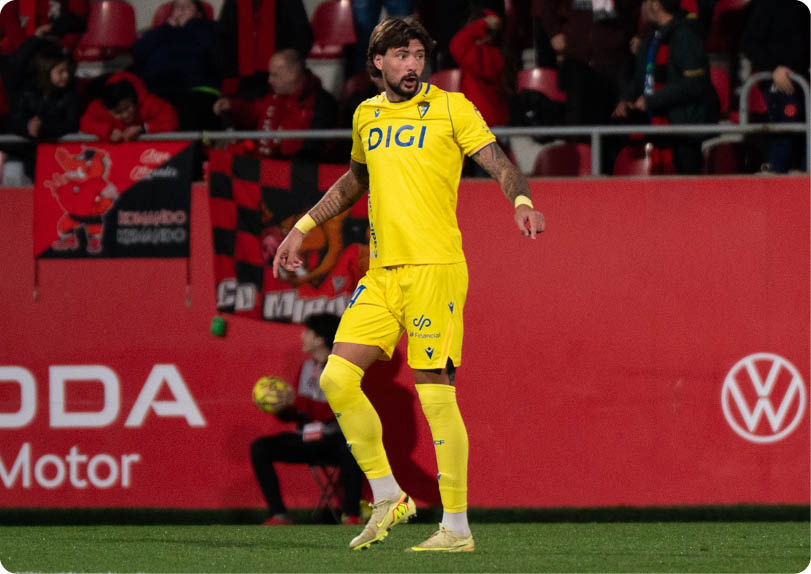A soccer player in a yellow and blue uniform stands on the field with his arms outstretched. Contenido generado con IA