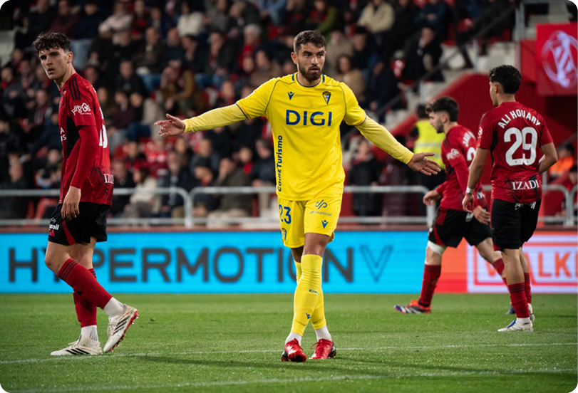 A soccer player in a yellow jersey stands on the field, looking up at the sky. Contenido generado con IA
