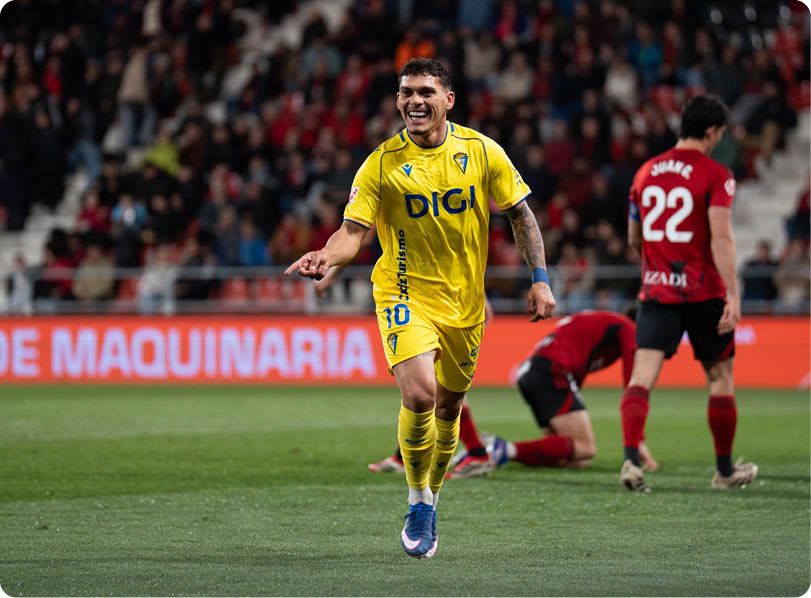 A soccer player in a yellow jersey is running on the field, smiling and pointing. Contenido generado con IA