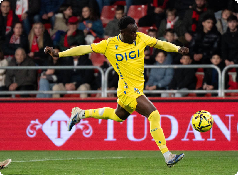 A soccer player in a yellow and blue uniform kicks a soccer ball on the field. Contenido generado con IA