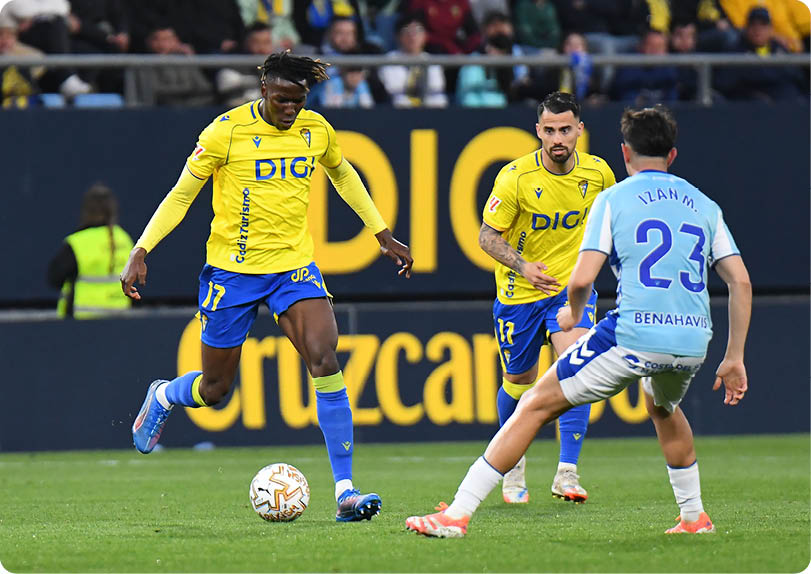 A man in a green jacket is walking on a field with a soccer ball. Contenido generado con IA