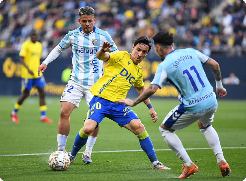 A soccer player in a yellow and blue uniform kicks a soccer ball on the field. Contenido generado con IA