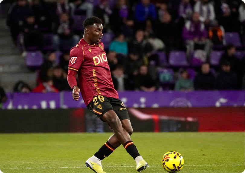 A soccer player in a red jersey is kicking a yellow and black soccer ball. Descripci n generada con IA