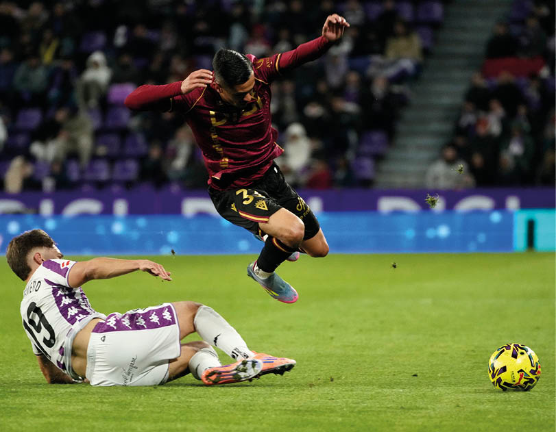 Two soccer players are on the field, one is kicking the ball and the other is falling. Descripci n generada con IA