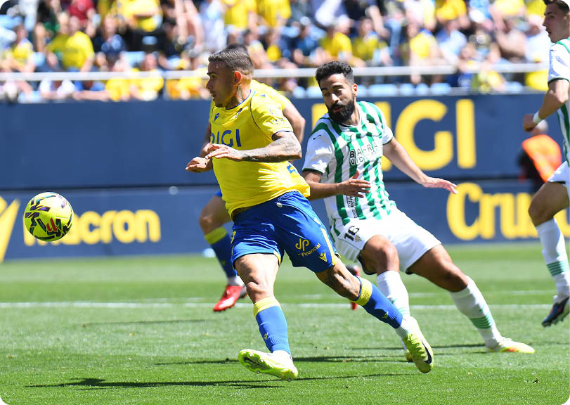 A soccer player in a blue uniform is running towards the ball. Descripci n generada con IA