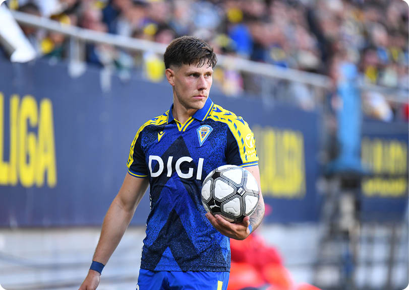 A soccer player in a blue uniform is running towards the ball. Descripci n generada con IA