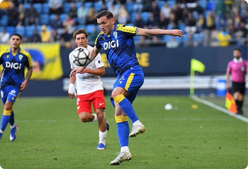 A soccer player in a blue and yellow uniform kicks a soccer ball. Descripci n generada con IA