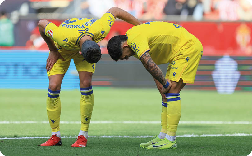 Two soccer players wearing yellow jerseys with blue stripes. Descripci n generada con IA