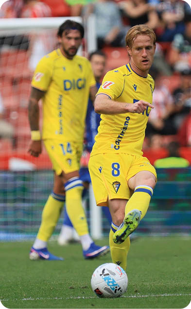A soccer player in a yellow and blue uniform is about to kick the ball. Descripci n generada con IA