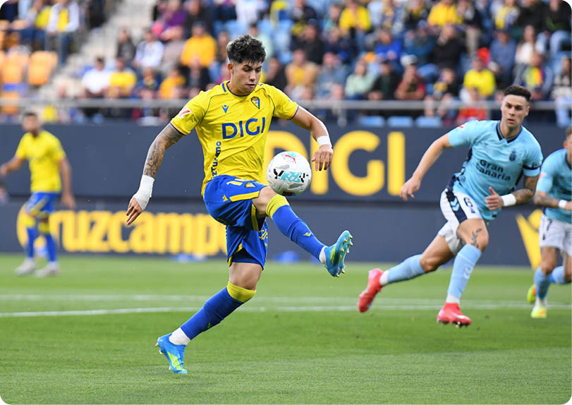 A soccer player in a yellow and blue uniform kicks a soccer ball. Descripci n generada con IA