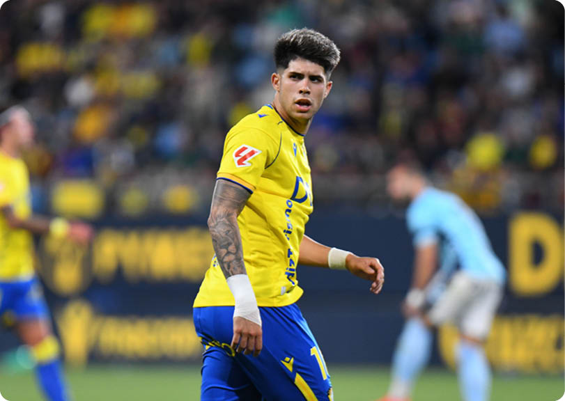 A soccer player with a yellow shirt and blue shorts. Descripci n generada con IA