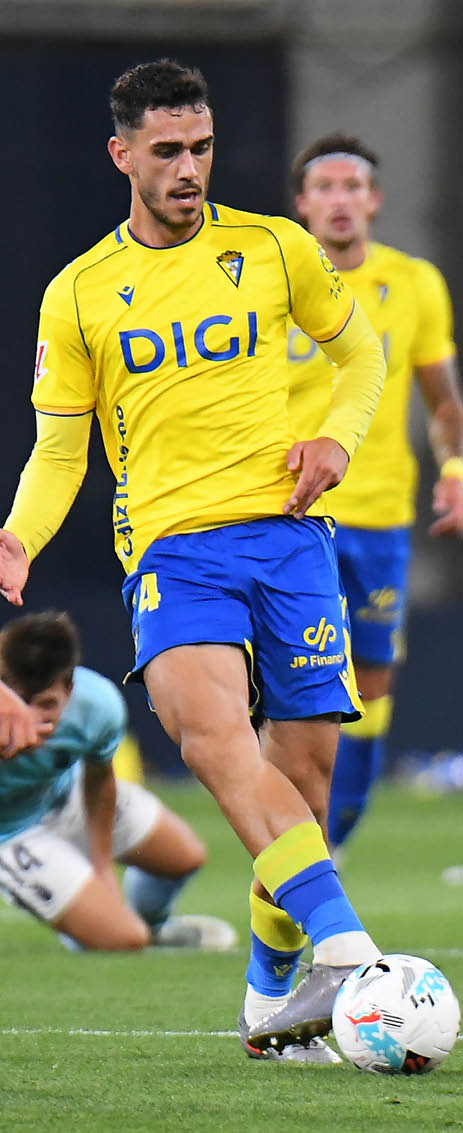 A soccer player in a yellow and blue uniform is kicking a soccer ball. Descripci n generada con IA