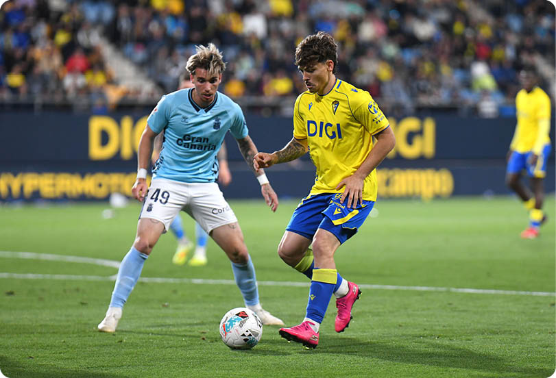 Two soccer players are playing on the field. Descripci n generada con IA