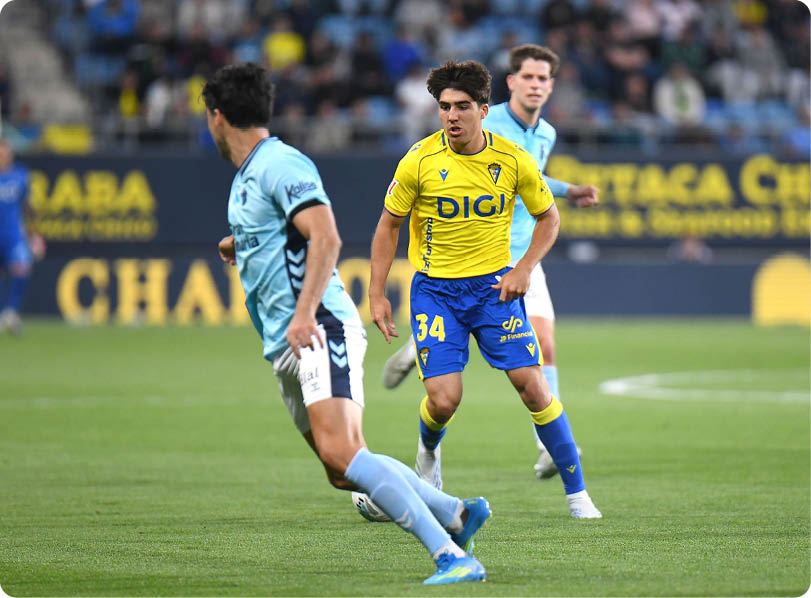 A soccer player in a blue shirt and yellow shorts is running on the field. Descripci n generada con IA