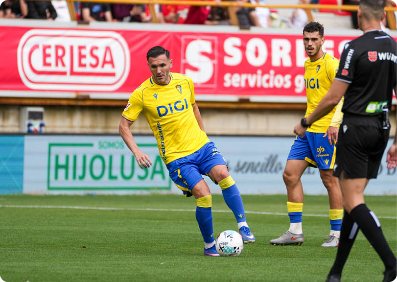 A soccer player in a yellow and blue uniform kicks a soccer ball. Descripci n generada con IA