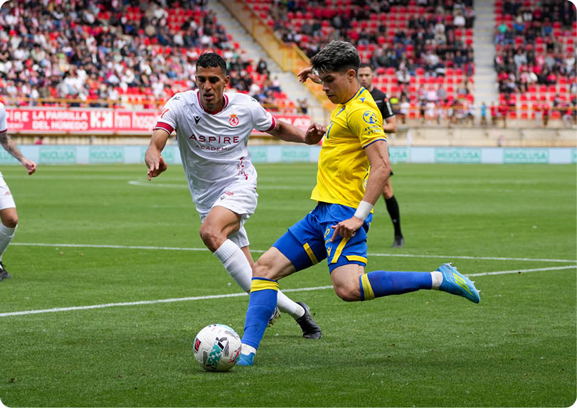 A soccer player in a yellow shirt and blue shorts is kicking a soccer ball. Descripci n generada con IA