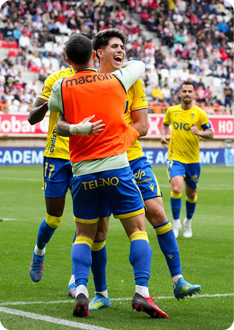 A group of men celebrating a goal on a soccer field. Descripci n generada con IA