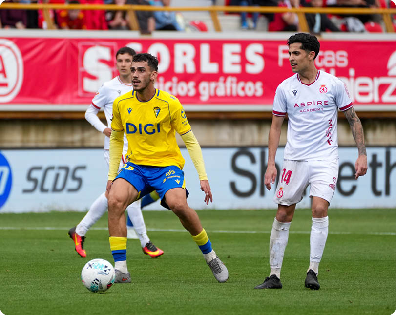 A soccer player in a yellow and blue uniform is kicking a soccer ball. Descripci n generada con IA