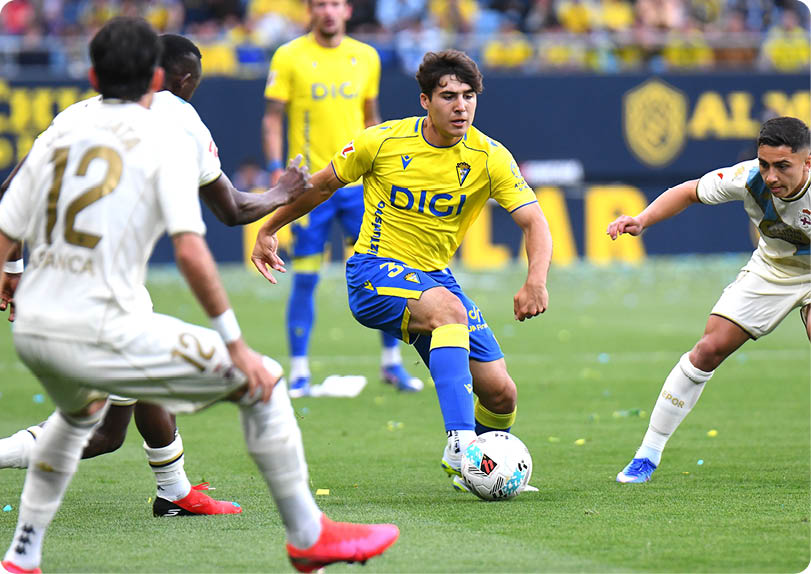 A soccer player in a yellow and blue uniform is running with the ball. Descripci n generada con IA