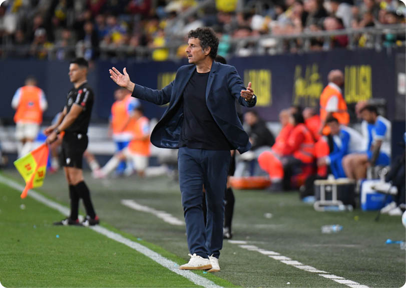 A man wearing a blue jacket and white shoes is standing on a field. Descripci n generada con IA