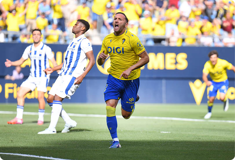 A soccer player in a yellow shirt and blue shorts is running on the field. Descripci n generada con IA