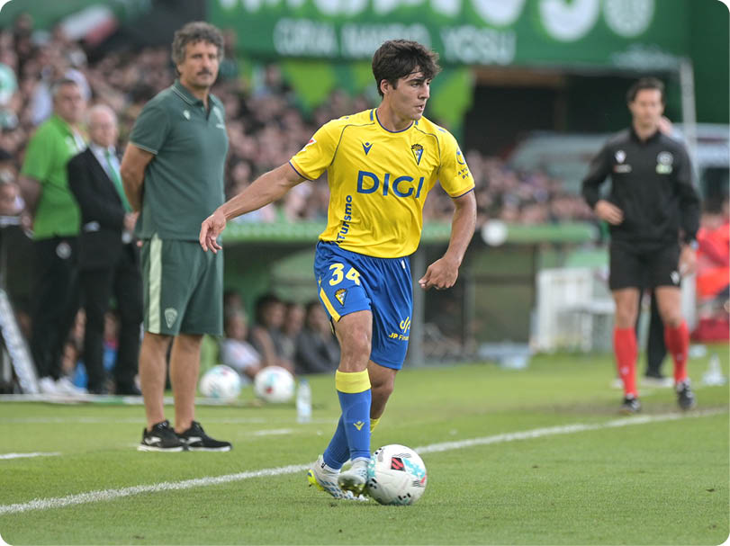 A soccer player in a yellow and blue uniform is kicking a soccer ball. Descripci n generada con IA