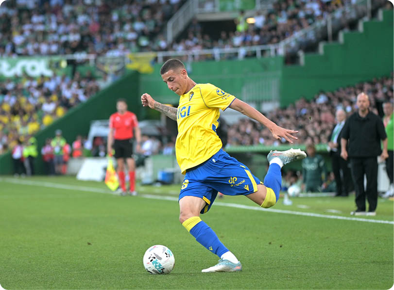 A soccer player in a yellow and blue uniform is kicking a soccer ball. Descripci n generada con IA