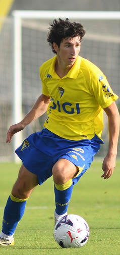 Persona con uniforme deportivo amarillo y azul jugando al f tbol en un campo. Descripci n generada con IA