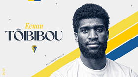 Persona con barba y cabello rizado corto vistiendo una camiseta blanca junto a un texto que dice Kenan Toibibou y un escudo deportivo. Descripci n generada con IA