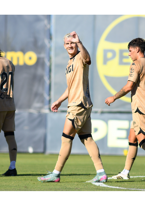 Personas con uniforme deportivo color beige est n en un campo de f tbol, una de ellas sonr e y hace un gesto con la mano mientras camina. Descripci n generada con IA