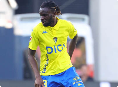 A person with braided hair wearing a yellow sports jersey with blue text is actively running outdoors. Descripci n generada con IA