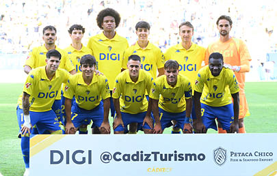 A group of adults wearing yellow and blue sports uniforms pose together on a field with a crowd in the background. Descripci n generada con IA