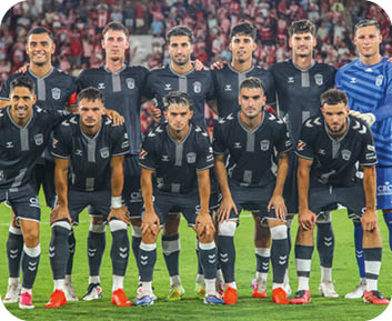 Un grupo de personas con uniformes deportivos celestes y blancos se abrazan y celebran en un campo de f tbol. Descripci n generada con IA