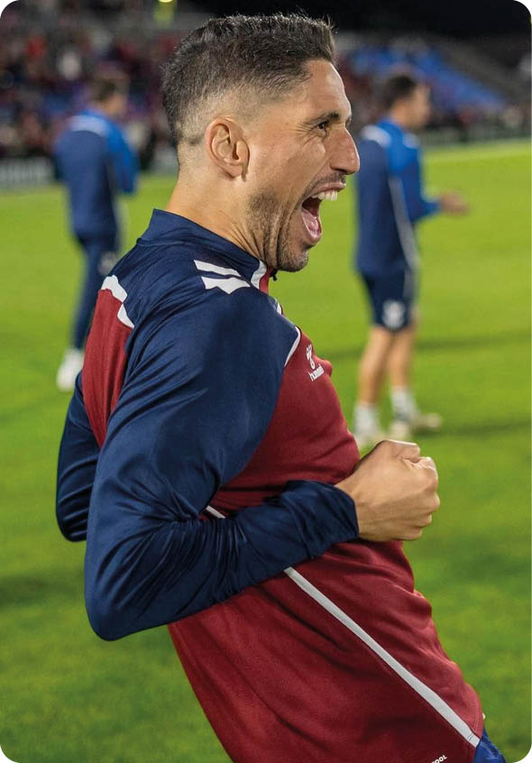 Una persona con camiseta deportiva roja y azul celebra con entusiasmo en un campo de f tbol durante un evento nocturno. Descripci n generada con IA