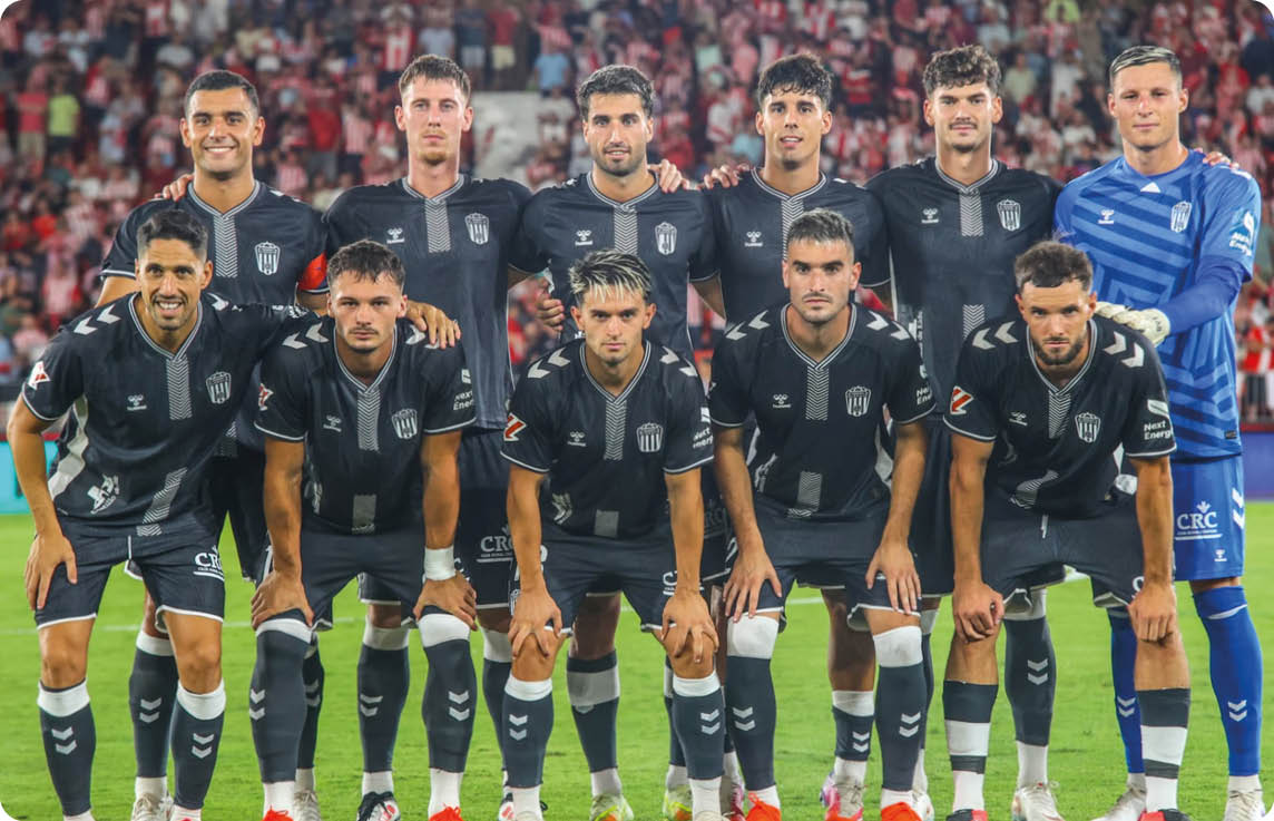 Un grupo de personas vestidas con uniformes deportivos posan en formaci n sobre un campo de f tbol con un estadio lleno de espectadores al fondo. Descripci n generada con IA