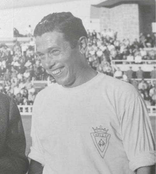 Dos personas con camisetas blancas posan juntas en un estadio deportivo con una multitud de fondo. Descripci n generada con IA