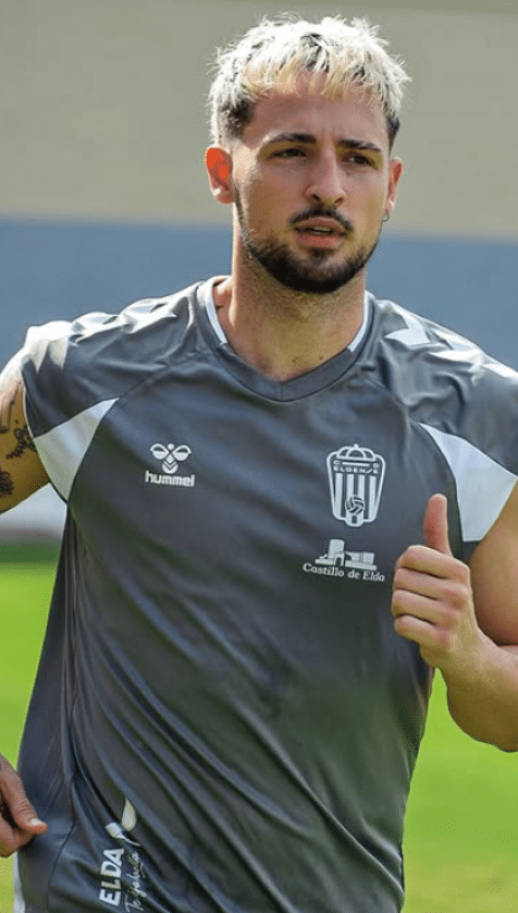 Persona con camiseta deportiva gris con logos y tatuajes visibles en el brazo, en un entorno al aire libre. Descripci n generada con IA