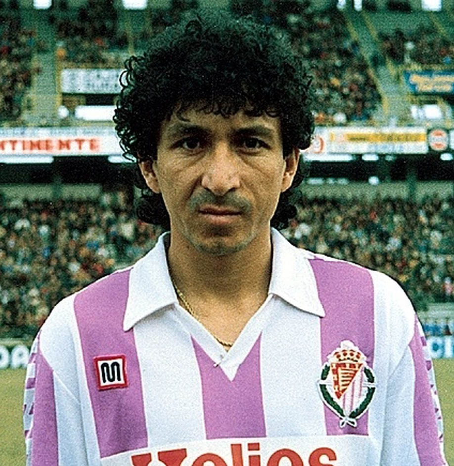 Persona con cabello rizado vistiendo uniforme deportivo de rayas blancas y moradas con el logo de Helios en un estadio con p blico al fondo. Descripci n generada con IA