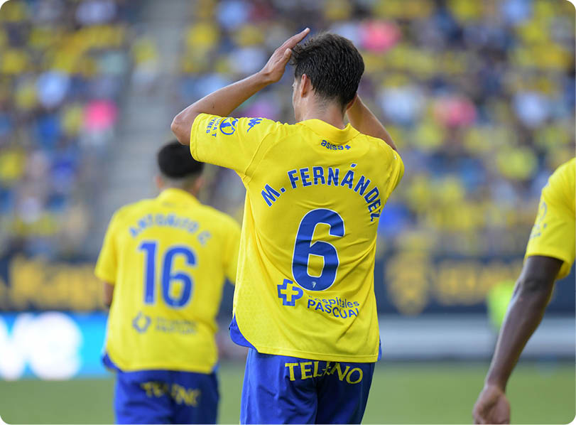 Three people wearing yellow and blue sports uniforms are on a field, with one person in the center holding their head and the others standing nearby. Descripci n generada con IA