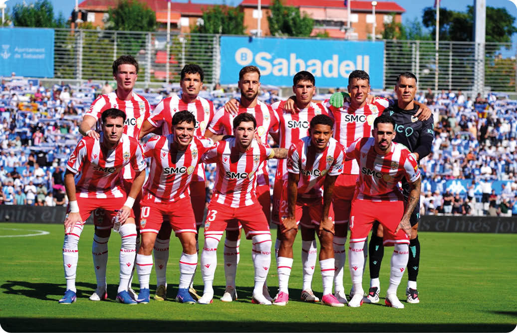 Un grupo de personas vestidas con uniformes deportivos a rayas rojas y blancas posan juntas en un campo de f tbol con un estadio lleno de espectadores al fondo. Descripci n generada con IA